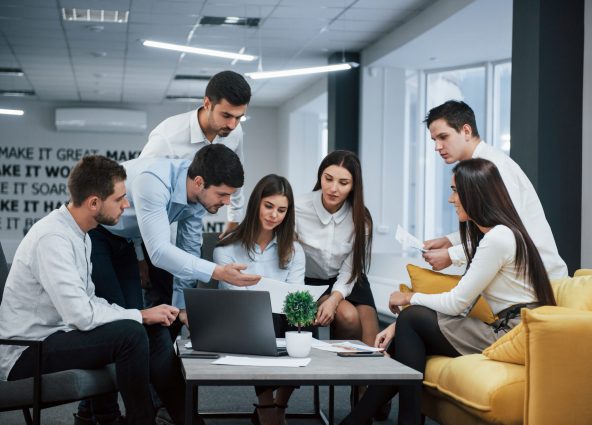 Guy shows document to a girl. Group of young freelancers in the office have conversation and working.